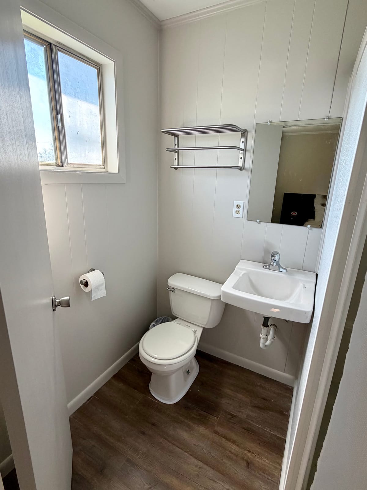 The Brewmaster's Room — private bathroom with toilet, pedestal sink, chrome towel rack, and window with natural light
