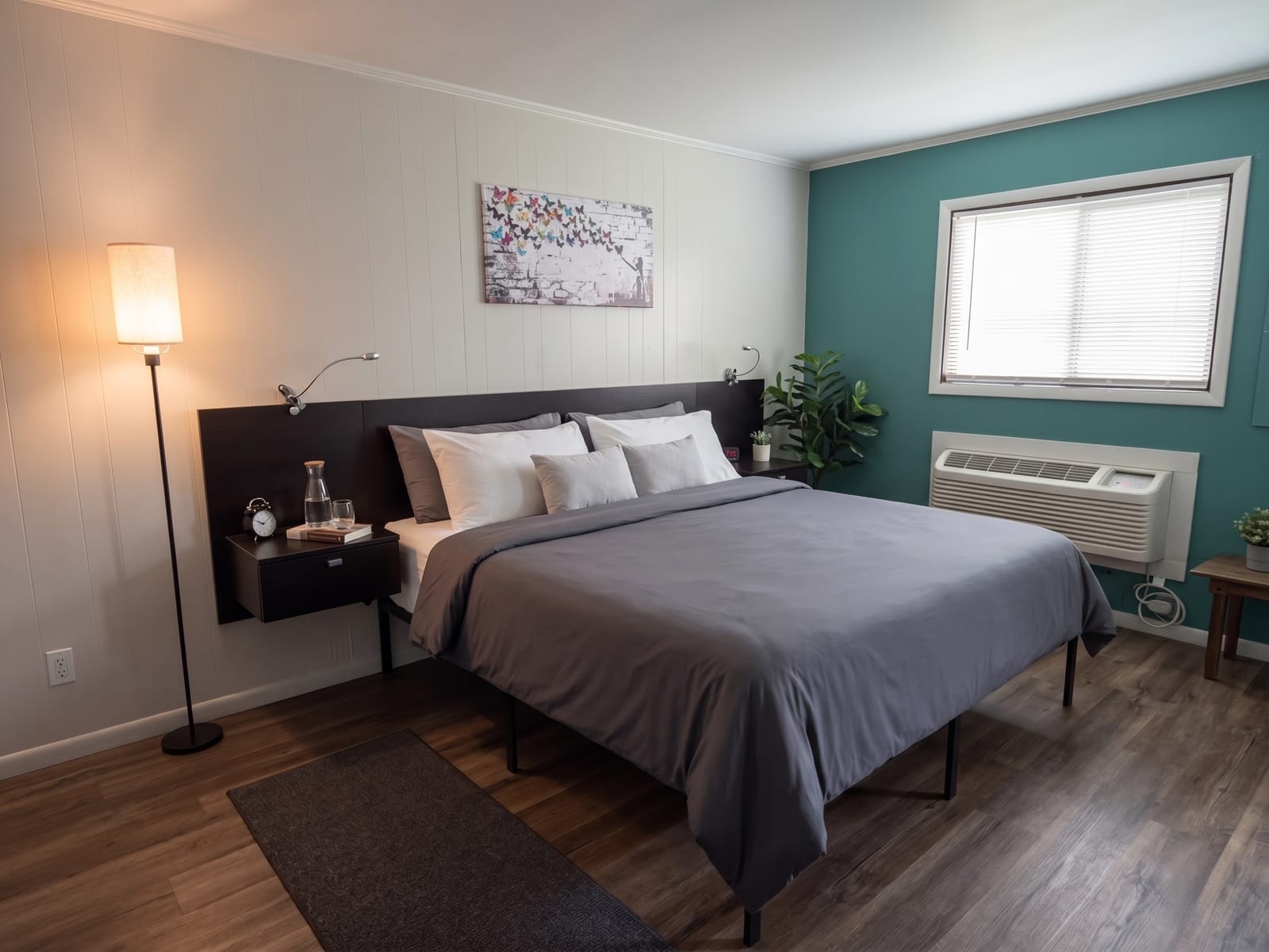 The Garden Room — king bed with gray bedding and dark headboard, vibrant butterfly mural artwork, and a teal accent wall