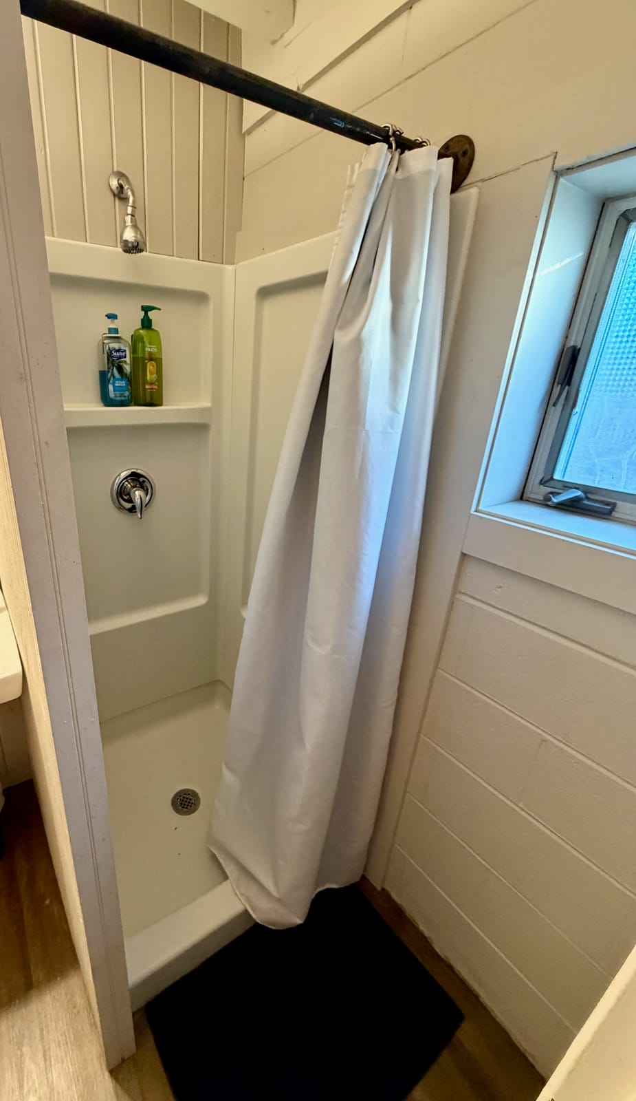 The Movie Room — private shower stall with white curtain, chrome fixtures, and natural light from window