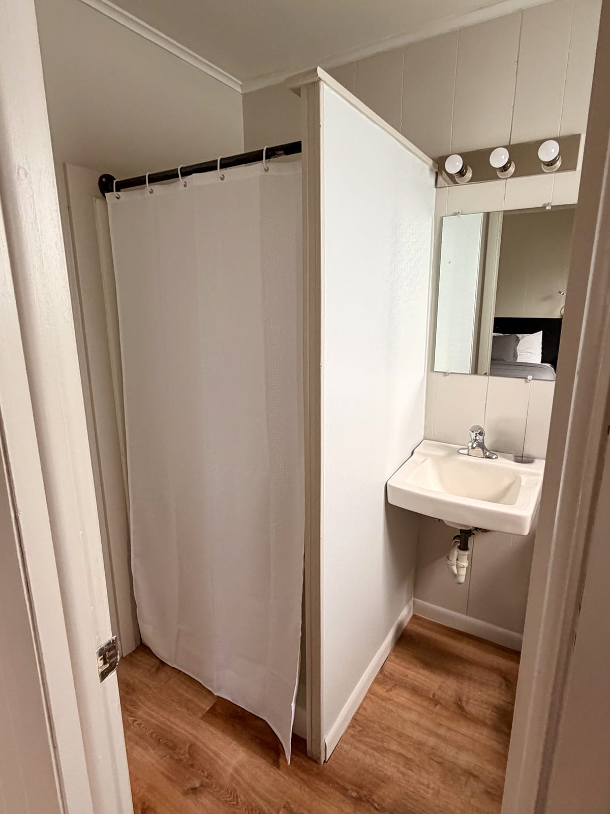 The Traveler's Den — private en-suite bathroom with shower, white curtain, and pedestal sink with vanity lights