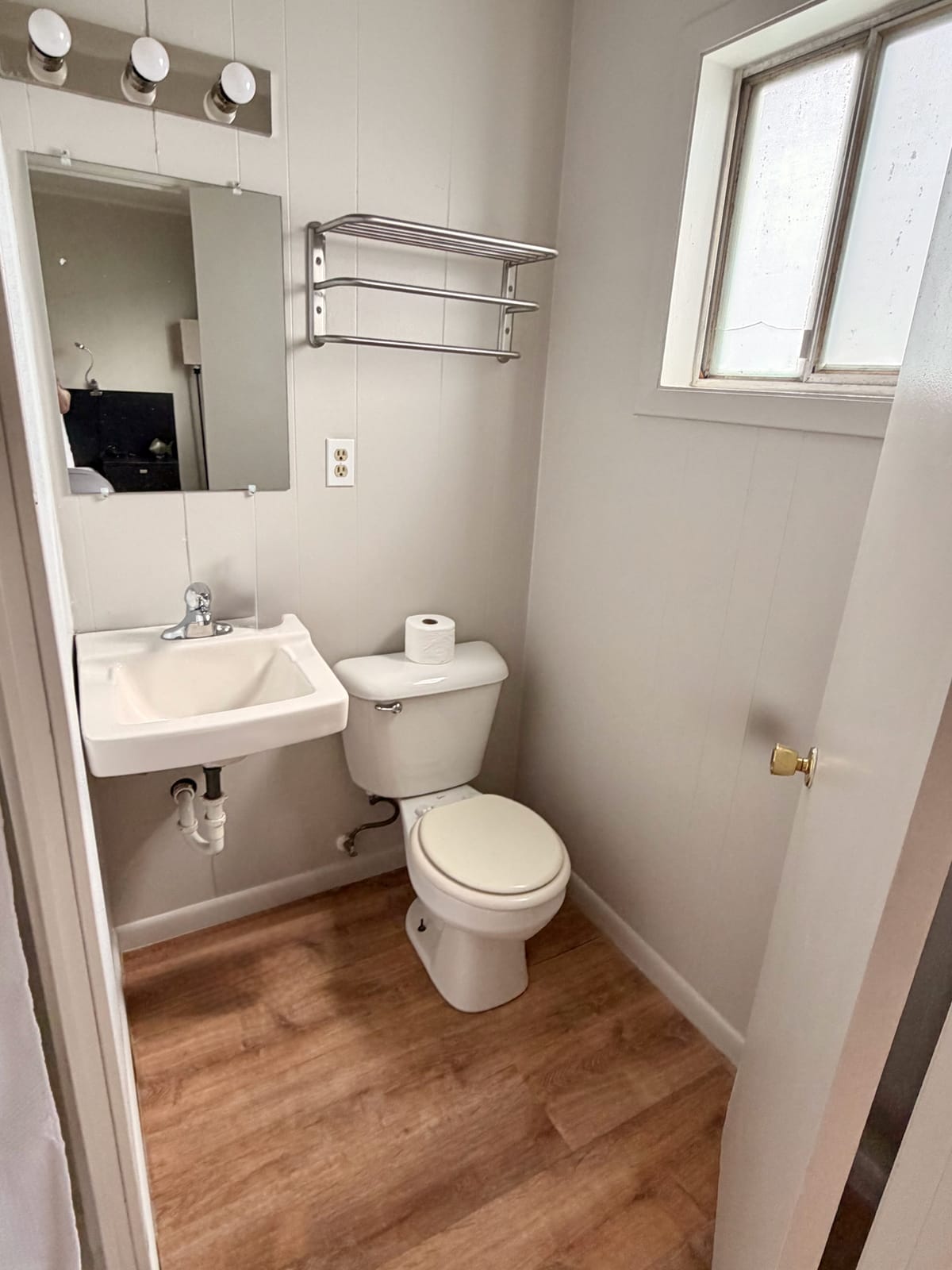 The Traveler's Den — private bathroom with pedestal sink, toilet, chrome towel rack, and bright window