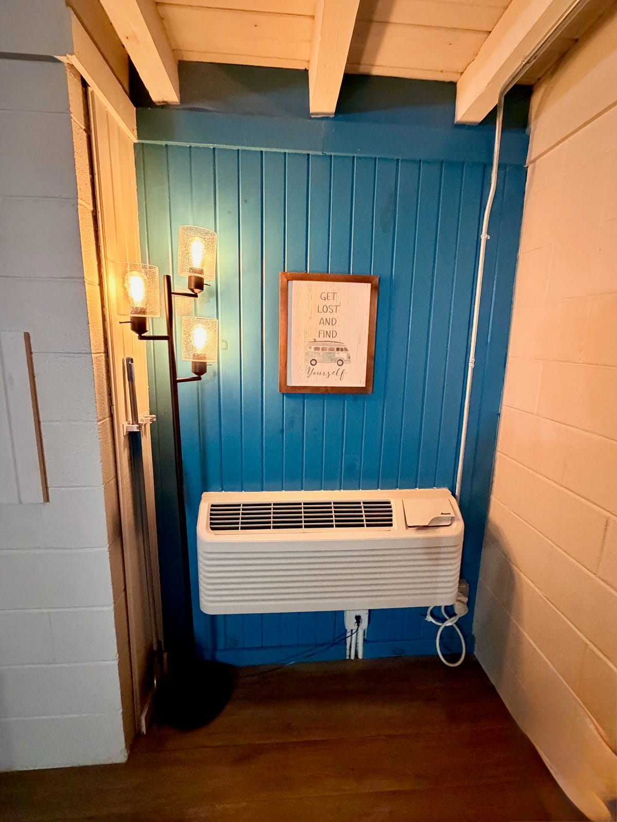 The Traveler's Den — cozy corner with industrial pendant floor lamp, framed wanderlust print, and teal blue accent wall