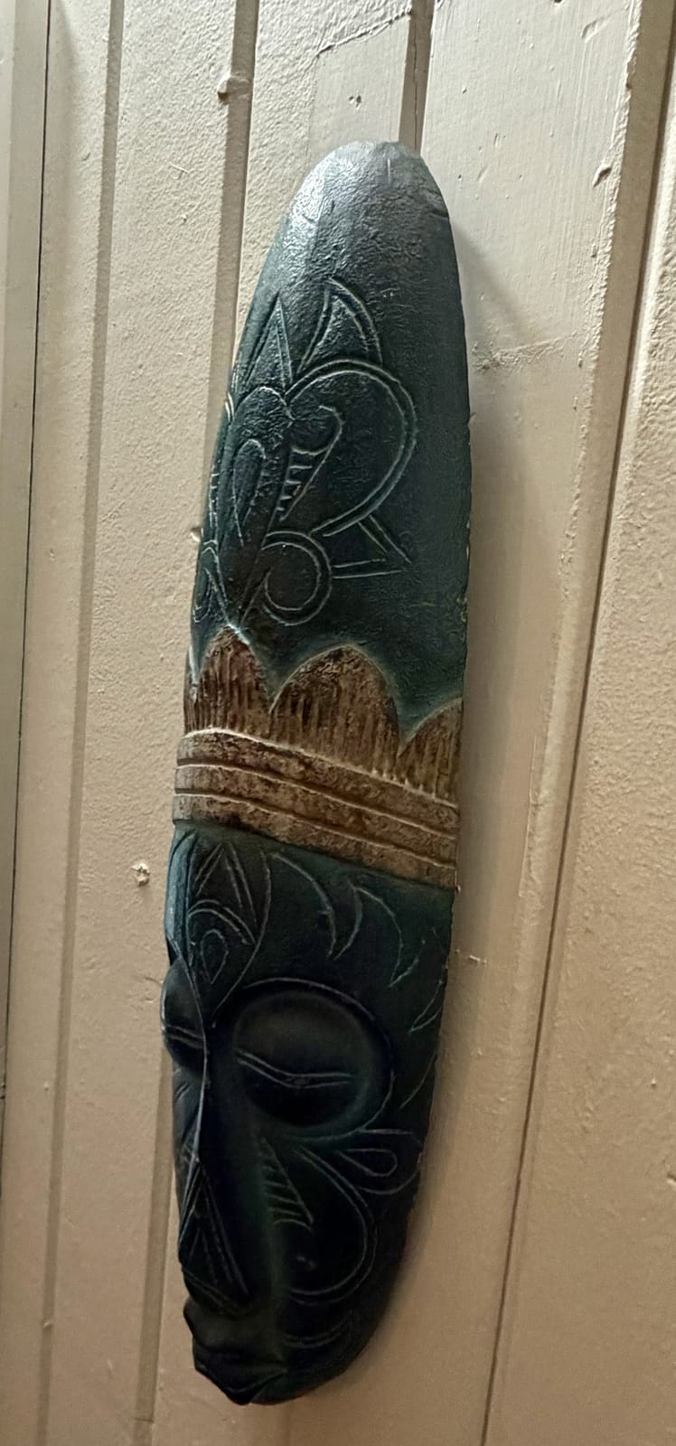 The Traveler's Den — hand-carved teal African-style wooden tribal mask on white paneled wall