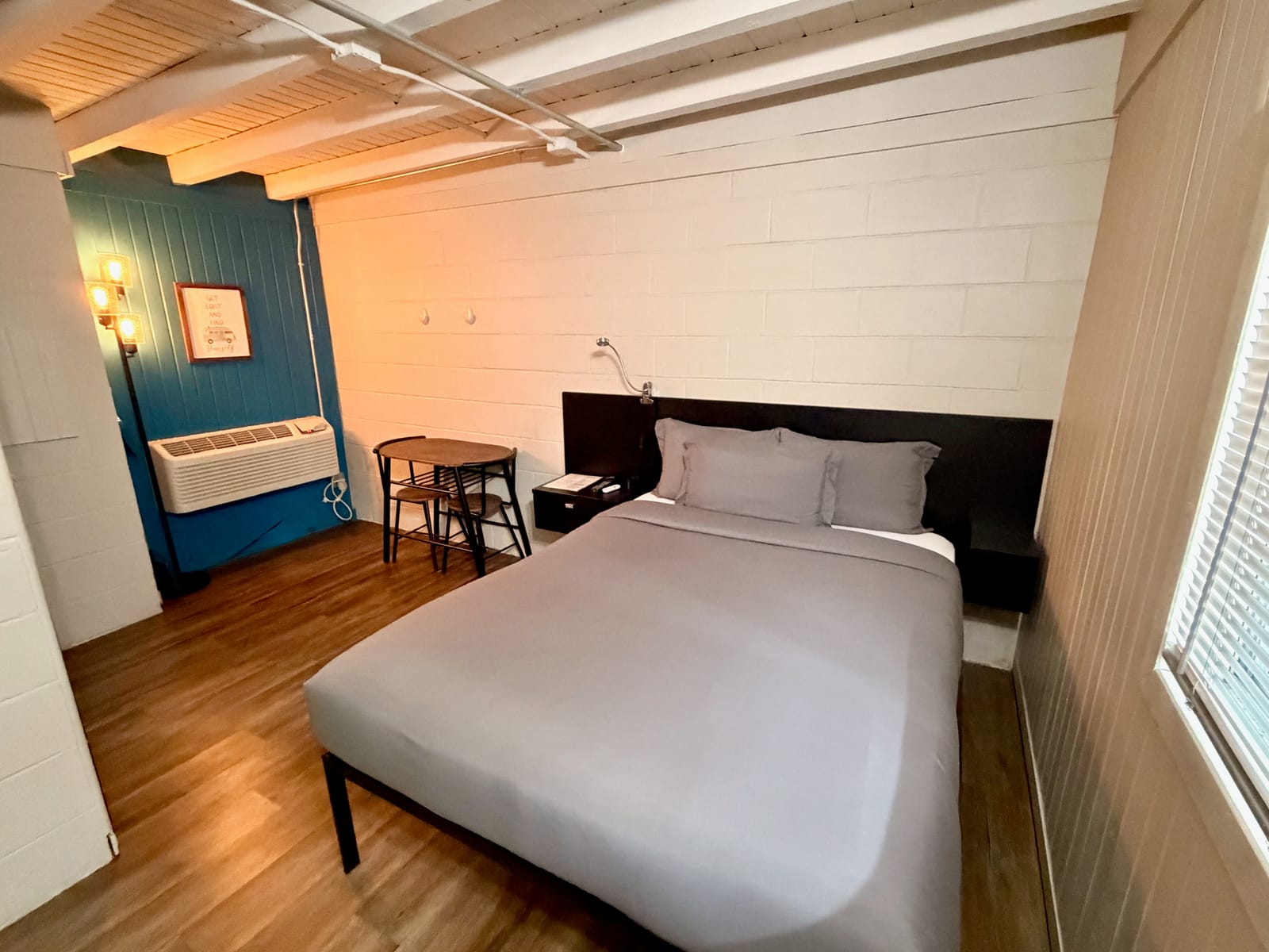 The Traveler's Den — king bed with dark headboard, vintage pendant lamps, bistro table, and exposed beam ceilings